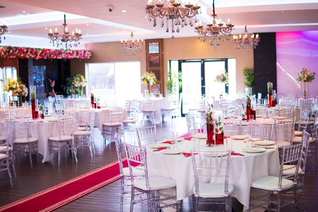 Event hall at The Maison Bradford with round tables, clear chairs, chandeliers, and floral décor used across weddings, parties, and corporate events.