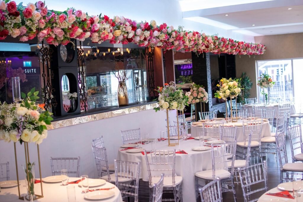 Wedding hall at The Maison Bradford with floral ceiling garlands, clear chairs, and round tables set for Asian weddings and Nikah ceremonies.