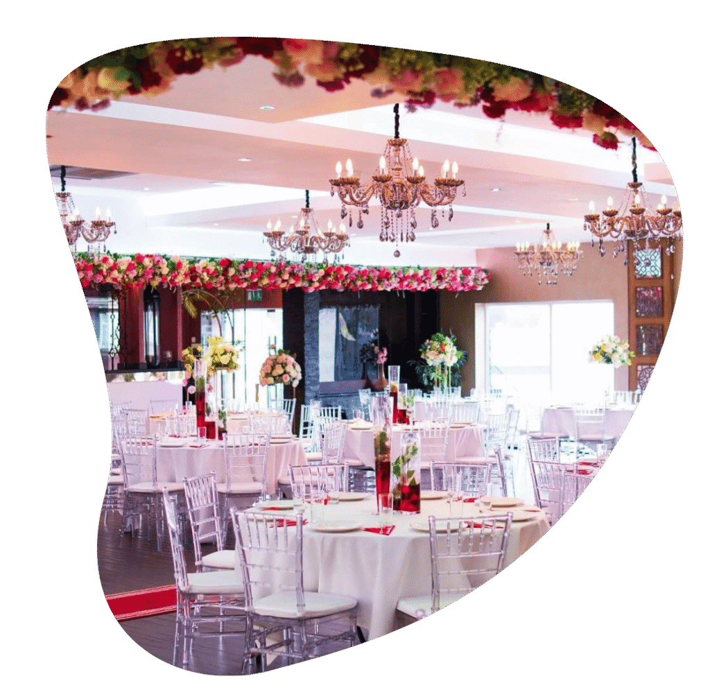 Event hall with round tables, clear chairs, floral ceiling décor and chandeliers at The Maison Bradford