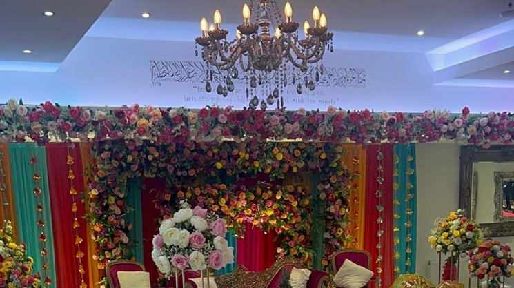 Asian wedding venue setup with colourful mehndi stage and round dining tables at The Maison Bradford